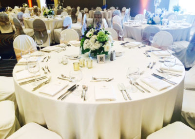 All white linens on round table with white covered chairs