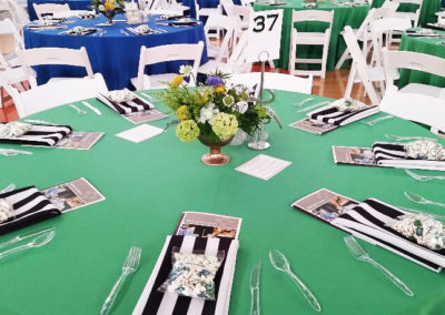 Green linens with striped napkins on round tables with white resin chairs