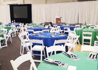 Blue and green linens on round tables with white resin chairs