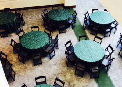Green linens on round tables with black resin chairs for corporate event
