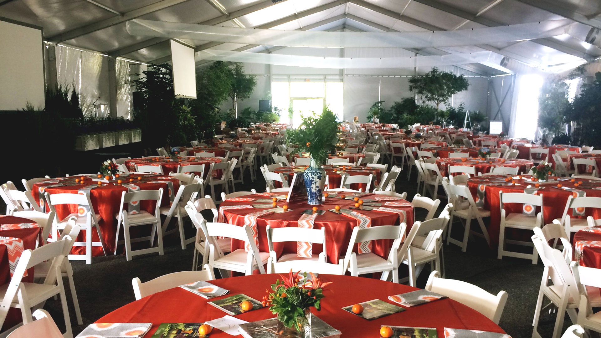 Corporate event with orange linens on round tables with white resin chairs
